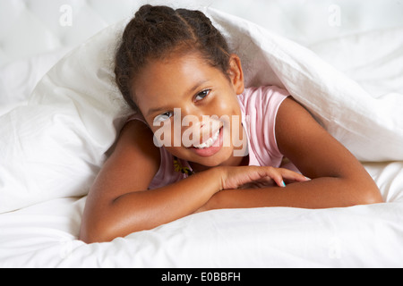 Jeune fille se cachant sous une couette dans le lit Banque D'Images