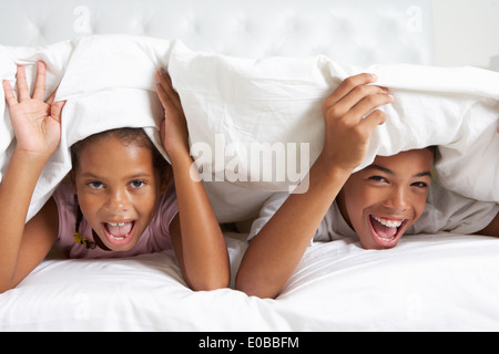 Deux enfants de se cacher sous une couette dans le lit Banque D'Images