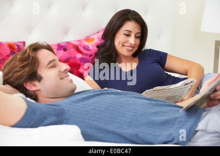 Couple Relaxing In Bed Wearing pajamas et Reading Newspaper Banque D'Images