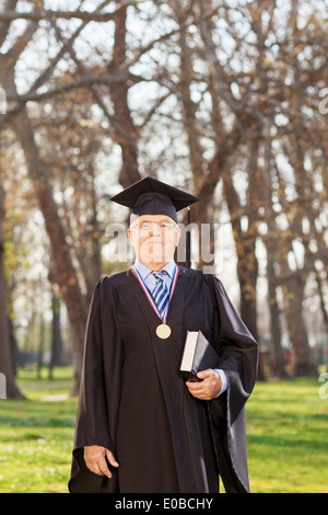 College doyen en graduation gown holding a book in a park Banque D'Images