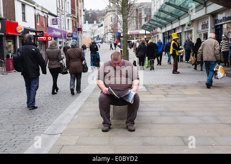 L'homme la lecture d'un document dans une rue commerçante animée. Banque D'Images