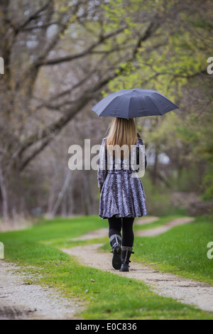 Femme fatale blonde marcher par elle-même sur un chemin de terre dans les bois avec un parapluie noir Banque D'Images