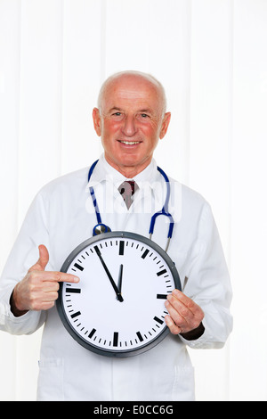 Un médecin est titulaire d'un réveil. Sur le Ziffernbaltt il est 5 minutes avant 12, Ein Arzt haelt eine Uhr. Es ist auf dem Ziffernbaltt 5 Mi Banque D'Images