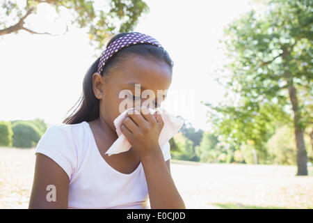 Little girl sitting on grass blowing her nose Banque D'Images