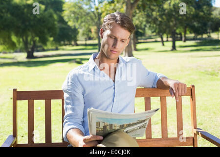 Handsome man sitting on park bench reading newspaper Banque D'Images