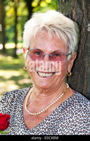 Heureux 74 ans avec une rose rouge., Froehliche aeltere Seniorin mit einer roten Rose. Banque D'Images