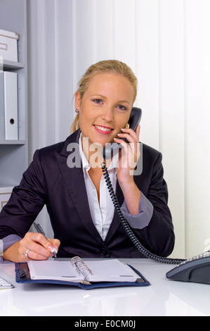 Une femme appelle à son bureau dans le bureau et prend les rendez-vous dans le calendrier Banque D'Images