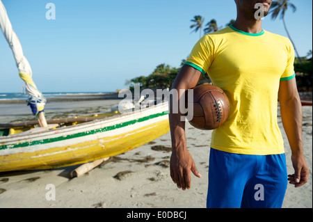 Joueur de football brésilien au Brésil couleurs vintage holding soccer ball en face du bateau de pêche sur la plage du Brésil Nordeste Banque D'Images