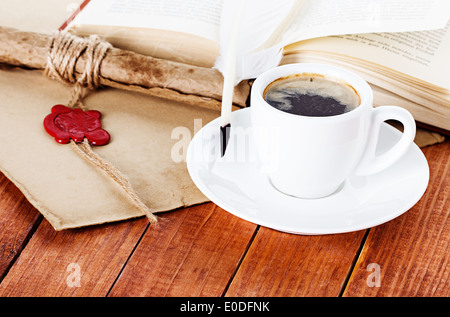 Tasse de café avec une plume et parchemin d'un livre sur fond de bois Banque D'Images