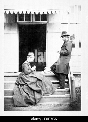 Photo vintage en noir et blanc d'un couple dans un escalier en milieu urbain, probablement prise à New York ou dans une ville voisine. L'image capture un moment historique avec le couple en vedette, mettant en valeur la mode et le style de vie au début du XXe siècle. Banque D'Images
