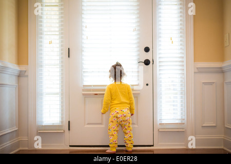 Petite fille en regardant par la fenêtre dans son pyjama. La lumière naturelle. Banque D'Images