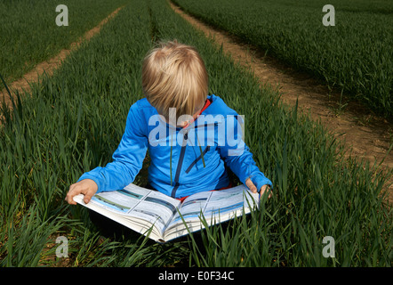 Libre d'un enfant garçon blond lisant un livre à l'extérieur dans un champ de blé, pelouse, jardin, cour, seul, l'étude Banque D'Images