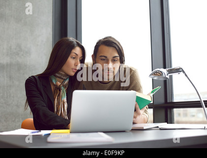 Les jeunes étudiants de l'université recherche d'informations dans des livres et un ordinateur portable pour leurs études. Assis à la table d'étudier ensemble. Banque D'Images