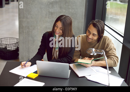 De jeunes étudiants à prendre des notes à partir de livres de référence pour l'étude. Jeune homme et femme assise à table avec des livres et l'ordinateur portable. Banque D'Images