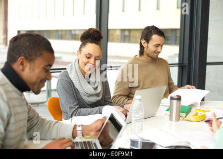 Young african american woman using laptop avec ses camarades de l'étude autour. Table de la bibliothèque de l'université avec des livres et l'ordinateur portable. Banque D'Images