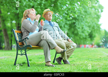 Couple de personnes âgées faisant des bulles dans le parc assis sur un banc Banque D'Images