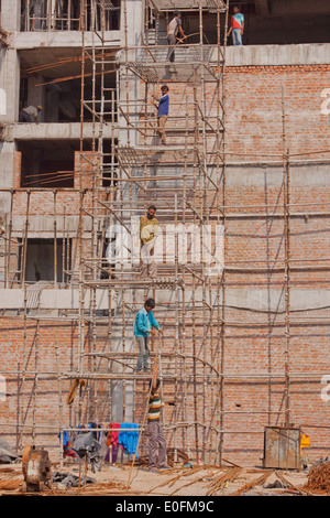 Les travailleurs forment une chaîne de montage de l'échafaudage en bois supplémentaire en haut d'un bâtiment en construction dans la région de Delhi, Inde Banque D'Images