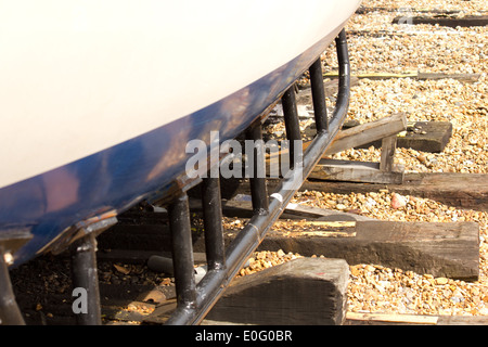 Bleu et blanc pris en charge coque de bateau avec des cales en bois sur une plage de bardeaux Banque D'Images