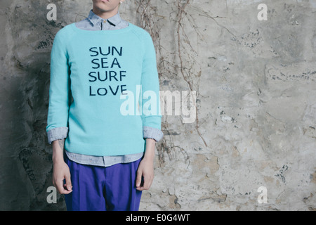 Jeune homme dans un milieu urbain, rêvant de la plage et de vouloir y aller, "Soleil, Mer, surf, Love' imprimé sur le chandail. Banque D'Images