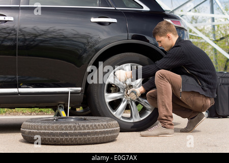 Jeune homme de changer le pneu crevé sur sa voiture le dévissage des écrous avec une clé de roue avant de soulever le véhicule Banque D'Images