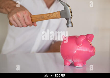 Businessman breaking piggy bank with hammer Banque D'Images