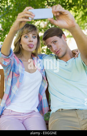 Drôle de couple assis sur un banc dans le parc en prenant un selfies Banque D'Images