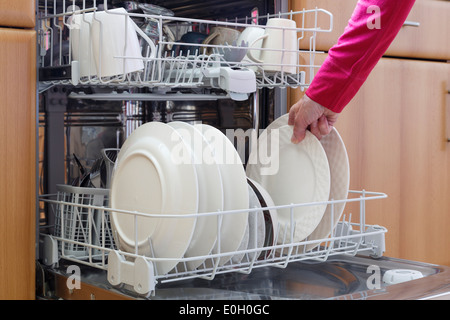 Scène quotidienne de tous les jours une femme de vidange d'un équipé d'un lave-vaisselle plein de nettoyer la vaisselle lavée dans une cuisine domestique à la maison UK, Grande-Bretagne Banque D'Images