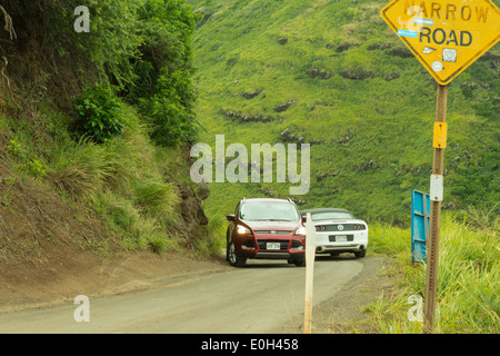 Deux voitures qui passent les uns les autres sur une étroite route côtière à l'Ouest de Maui, Hawaii, avec road panneau disant route étroite. Banque D'Images