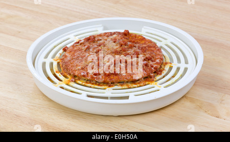 Une petite pizza au pepperoni, qui a été trop cuit dans un four micro-ondes sur un comptoir en bois. Banque D'Images