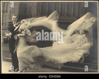 Cette photographie capture le mariage de Cyril Ritchard et Madge Elliott à la cathédrale de Sécession Mary à Sydney. Le voile et le train de la mariée sont soufflés par le vent, mettant en valeur un moment d'élégance et de grâce le jour de leur mariage en 1935. Banque D'Images