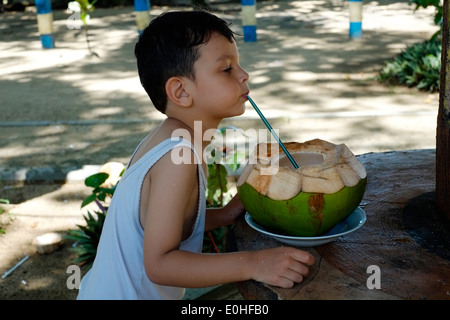 Jeune garçon de boire à partir de noix de coco fraîche par la plage et la mer à l'Est de Java, Indonésie balekambang Banque D'Images