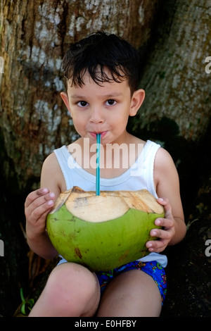 Jeune garçon de boire à partir de noix de coco fraîche par la plage et la mer à l'Est de Java, Indonésie balekambang Banque D'Images