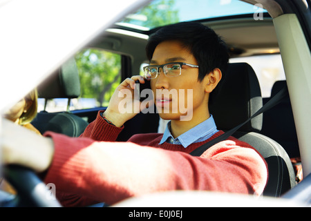 Young Asian man driving car and talking on mobile phone Banque D'Images