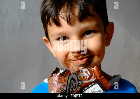 Jeune garçon mangeant une glace au chocolat et obtenir la plupart d'il enduit sur son visage Banque D'Images