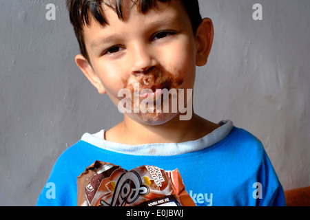 Jeune garçon mangeant une glace au chocolat et obtenir la plupart d'il enduit sur son visage Banque D'Images