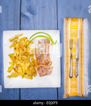 Pommes de terre sautées avec du hareng et l'oignon dans la plaque carrée blanche, d'étoffe jaune ,couteau et fourchette, servir sur table en bois bleu Banque D'Images