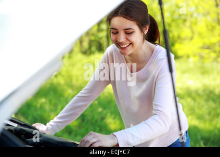 Smiling woman looks sous capot voiture contexte green park Banque D'Images