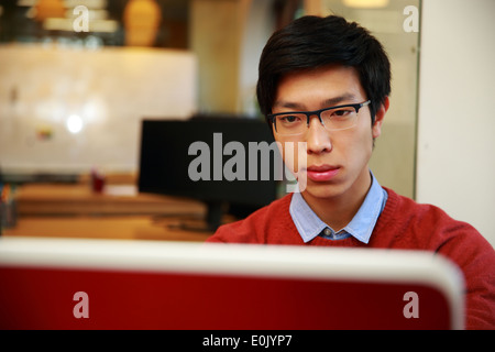 Young Asian man dans les verres working on laptop Banque D'Images