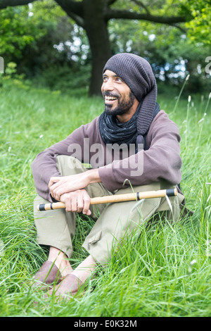 Mixed Race man playing flute dans l'herbe longue sur Hampstead Heath portant des vêtements amples et foulard Banque D'Images