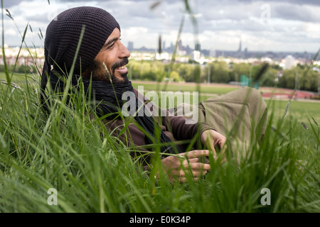 Mixed Race man se détendre dans l'herbe longue sur Hampstead Heath portant des vêtements amples et foulard Banque D'Images