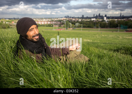 Mixed Race man se détendre dans l'herbe longue sur Hampstead Heath portant des vêtements amples et foulard Banque D'Images