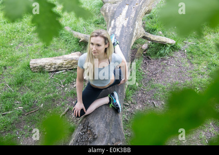 Dame blonde portant des guêtres noires et un top gris practicing yoga on a log sur Hampstead Heath. Banque D'Images