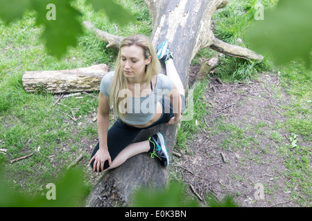 Dame blonde portant des guêtres noires et un top gris avec les yeux fermés la pratique du yoga sur un journal sur Hampstead Heath. Banque D'Images