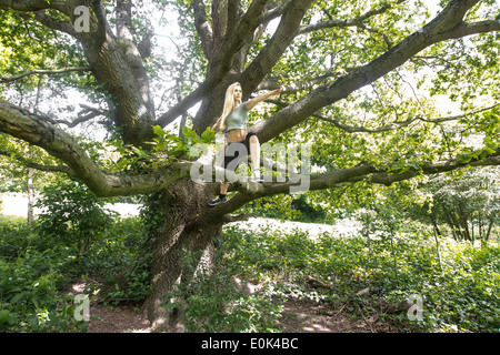 Dame blonde portant des guêtres noires et un top gris la pratique du yoga dans un arbre, à Hampstead Heath. Banque D'Images