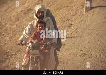 Un Afghan homme porte à la fois sa fille et sa femme sur une moto comme ils à travers la brume poussiéreuse de Kandahar, Afghanistan, Banque D'Images