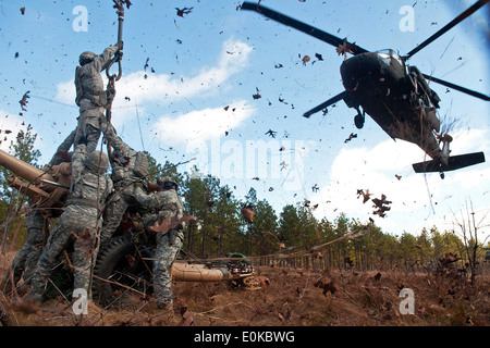 Les feuilles et les brindilles sont fouettés dans l'air par le souffle du rotor de l'hélicoptère UH-60 Black Hawk que des soldats se préparent à accrocher un M1 Banque D'Images