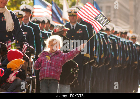 Un enfant d'un nouveau service de la Garde côtière de la région de New York états vagues le drapeau américain tout en marchant dans la ville de New York la Journée des anciens combattants de la Pa Banque D'Images