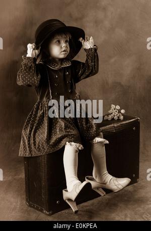 Quatre-année-vieille fille bébé en robe vintage assis sur la valise. Nom original : 'Mautres chaussures femme, grand-mère hat'