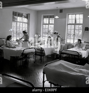 Historique des années 1950. Un lumineux et bien éclairé de la maternité de l'hôpital avec les mères dans la récupération après la naissance métal lits surveillés par des infirmières et d'une femme sur le point de tenir son enfant nouveau-né. Banque D'Images