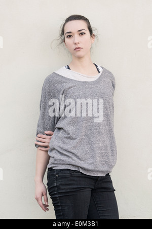 Portrait of a young woman standing in front of wall. Elle a une expression pensive et est à la recherche à l'appareil photo. Banque D'Images